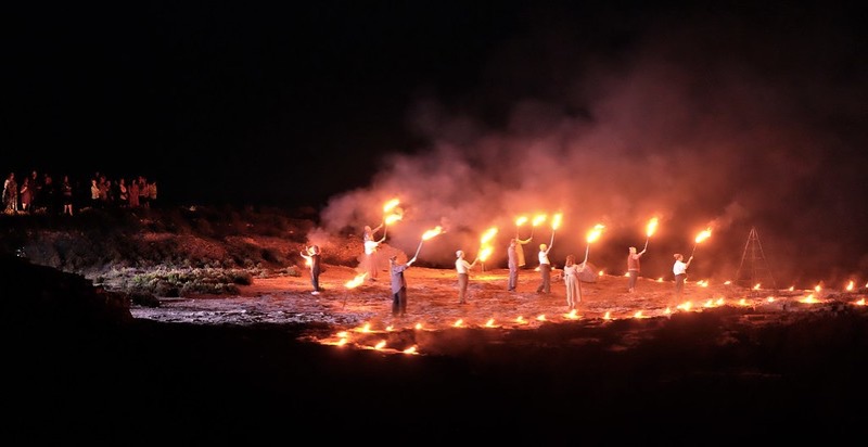 Performers holding flaming torches in a quarry at night